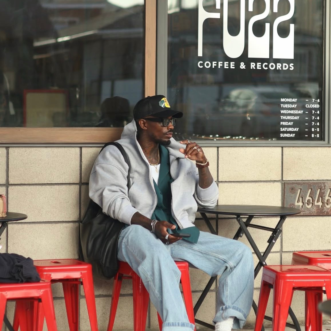 fashion man sit at a terrasse wearing monateo jewelry, a cap, sunglasses